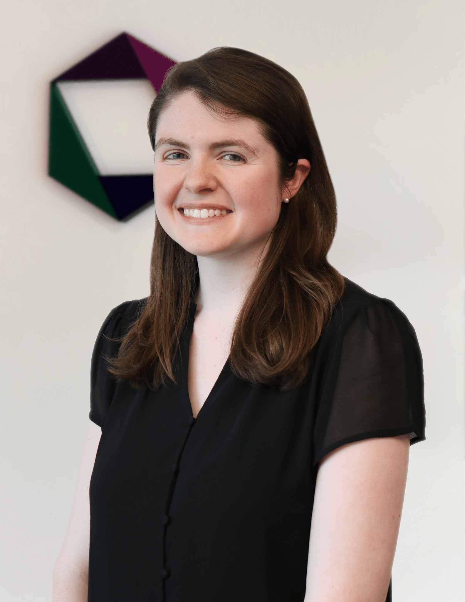 Ben Kass smiles at the camera while standing in front of the EK logo.